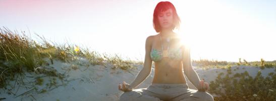 Bild på en kvinna som sitter på stranden och mediterar. Bilden illustrerar att det går att koppla av och leva som vanligt även när du har mens.