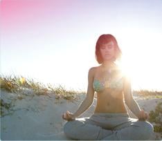 Bild på en kvinna som sitter på stranden och mediterar. Bilden illustrerar att det går att koppla av och leva som vanligt även när du har mens.